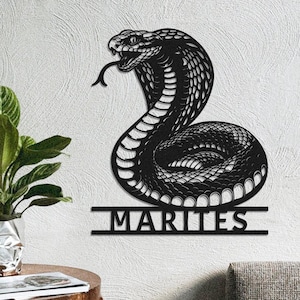 Könnte beinhalten: Schwarze Metall-Wandkunst einer Kobra-Schlange mit herausgestreckter Zunge. Die Schlange ist eingerollt und hat detaillierte Schuppen. Das Wort "MARITES" wird darunter angezeigt.
