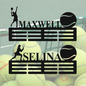 以下が含まれることがあります： 「MAXWELL」と「SELINA」の名前が入った、黒い金属製のテニスをテーマにした壁の装飾。各作品にはテニス選手のシルエット、テニスボール、水平バーのデザインが含まれています。背景にはテニスボールが写っています。