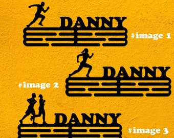 May include: Black metal medal display rack with the name "DANNY" and a silhouette of a runner. The rack has multiple horizontal bars for hanging medals.