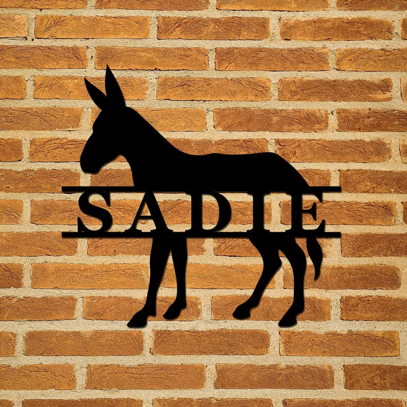 May include: Black metal silhouette of a donkey with the name "SADIE" cut out in the middle of the animal. The silhouette is mounted on a brick wall.