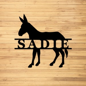 May include: Black silhouette of a donkey with the name "SADIE" in a split-style design. The name is centered on the donkey's body, with a line above and below the name.