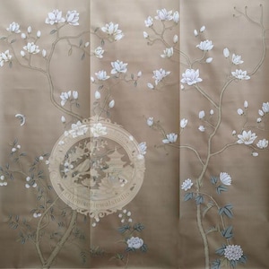 Könnte beinhalten: Beige Wandverkleidung mit floralem Design. Weiße Magnolienblüten und grüne Blätter schmücken die Zweige. Ein kreisförmiges Emblem mit asiatisch inspirierten Bildern befindet sich in der Mitte der Wandverkleidung.
