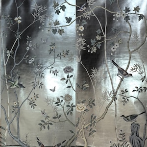 May include: Silver wallpaper with a detailed botanical design. The wallpaper features stylized trees, flowers, and birds in shades of gray, white, and green. Butterflies add a delicate touch to the overall aesthetic. The background has a metallic sheen.