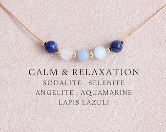 May include: A delicate necklace featuring five round gemstone beads in shades of blue and white, separated by small gold-toned spacers on a thin cord. The text CALM & RELAXATION SODALITE . SELENITE ANGELITE . AQUAMARINE LAPIS LAZULI is printed below.