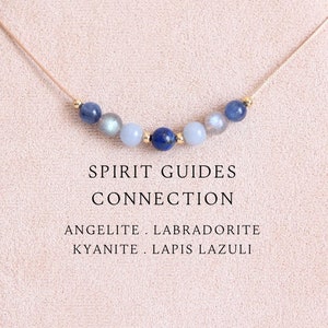 May include: A delicate necklace featuring a thin cord strung with seven small round beads in shades of blue, grey, and gold, including lapis lazuli, labradorite, kyanite, and angelite. The text reads SPIRIT GUIDES CONNECTION ANGELITE . LABRADORITE KYANITE . LAPIS LAZULI.