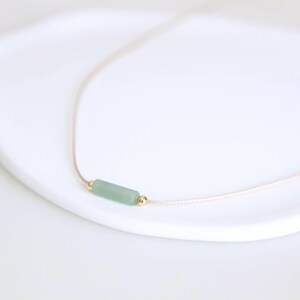 May include: A delicate necklace with a light green stone bar pendant and gold accents.
