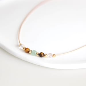 May include: A delicate gold chain necklace with a row of small beads in various colors, including clear, green, brown, and gold.