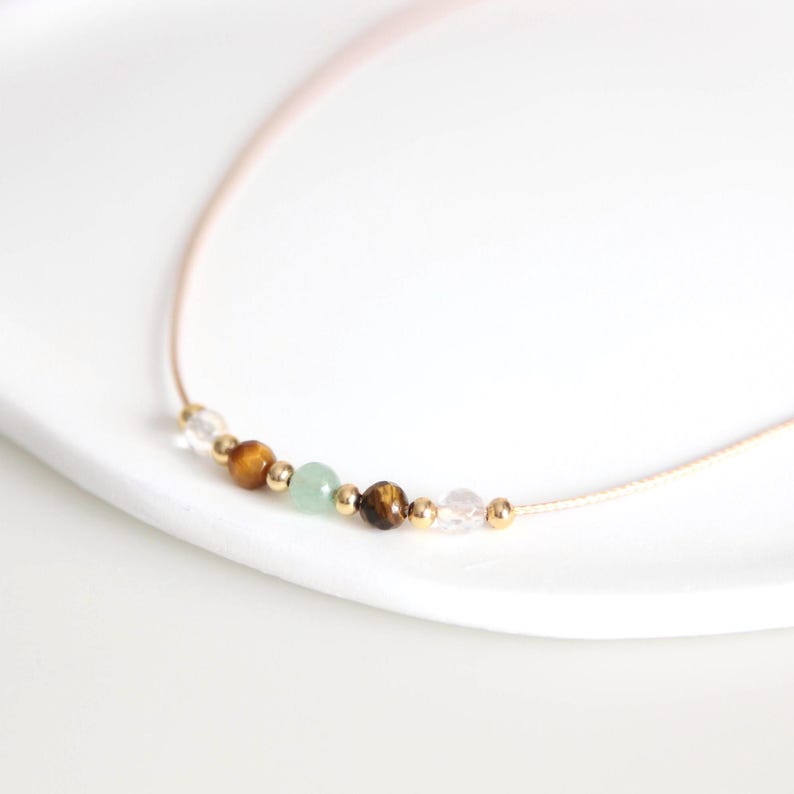 May include: A delicate gold chain necklace with a row of small beads in various colors, including clear, green, brown, and gold.