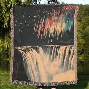 May include: A woven tapestry featuring a colorful aurora borealis and a waterfall. The tapestry is dark blue with streaks of pink, orange, green, and blue. The waterfall is white and cascading down a dark cliff.
