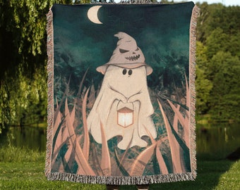 Puede incluir: Una manta de tejido de estilo tapiz con un fantasma de dibujos animados que lleva un sombrero de bruja y sostiene una linterna. El fantasma es blanco y el fondo es verde oscuro con una luna creciente.