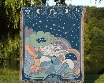 Könnte beinhalten: Eine gewebte Wandteppich mit einem blauen Hintergrund, einem weißen Sternzeichen Steinbock, Sternen und einem Regenbogen. Der Wandteppich ist mit Fransen versehen und hat das Wort "Steinbock" unten.