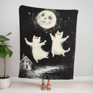 May include: Black and white illustration of two white cats flying in the air with a smiling moon in the background. The cats are silhouetted against a dark night sky with stars. A small house is visible in the foreground.
