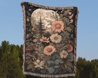 May include: A tapestry woven with a full moon, a forest scene, and a variety of flowers in shades of pink, yellow, and white. The tapestry is dark blue with a fringe border.