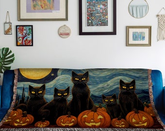 Puede incluir: Una manta tejida con un tema de Halloween con gatos negros y calabazas. La manta tiene un fondo de noche estrellada con una luna grande y una ciudad en la distancia.