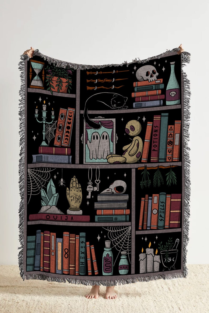 Op de afbeelding: Een zwart en grijs geweven wandkleed met een boekenkastontwerp. De boekenkast is gevuld met boeken, drankjes, kaarsen en andere magische voorwerpen. De tekst "OUIJA", "SPELLS" en "POTIONS" is zichtbaar op de boeken.