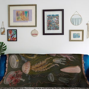 May include: A tapestry throw blanket with a dark green background featuring a vintage illustration of jellyfish in shades of pink, white, and brown.
