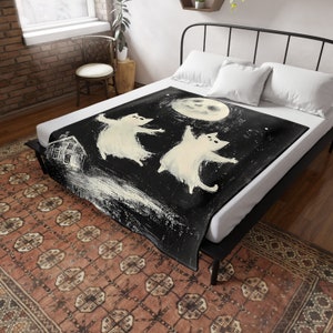 May include: Black and white fleece blanket with a whimsical illustration of two white cats dancing under a full moon. The cats are stylized and have a cartoonish appearance. The moon is a simple circle with a face.