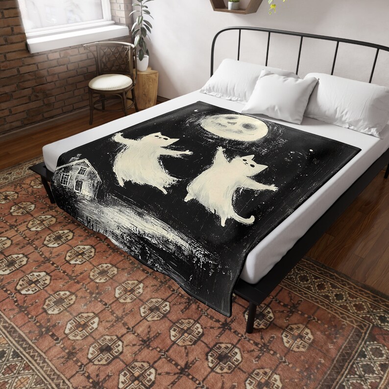 May include: Black and white fleece blanket with a whimsical illustration of two white cats dancing under a full moon. The cats are stylized and have a cartoonish appearance. The moon is a simple circle with a face.