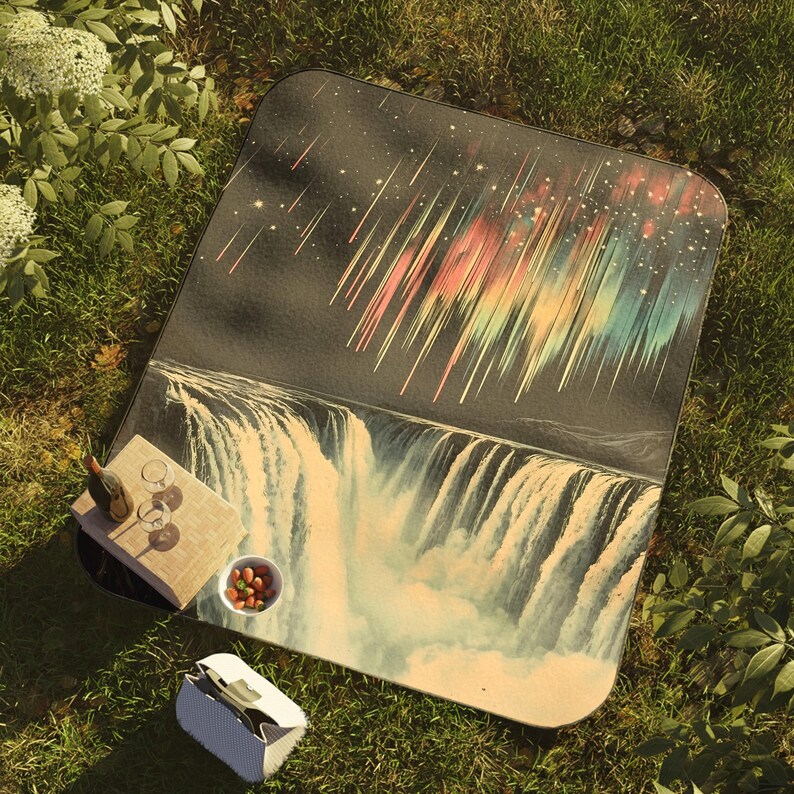 May include: A picnic blanket with a colorful aurora borealis and waterfall design. The blanket is laid out on green grass with a wine bottle, glasses, and a bowl of nuts on top.