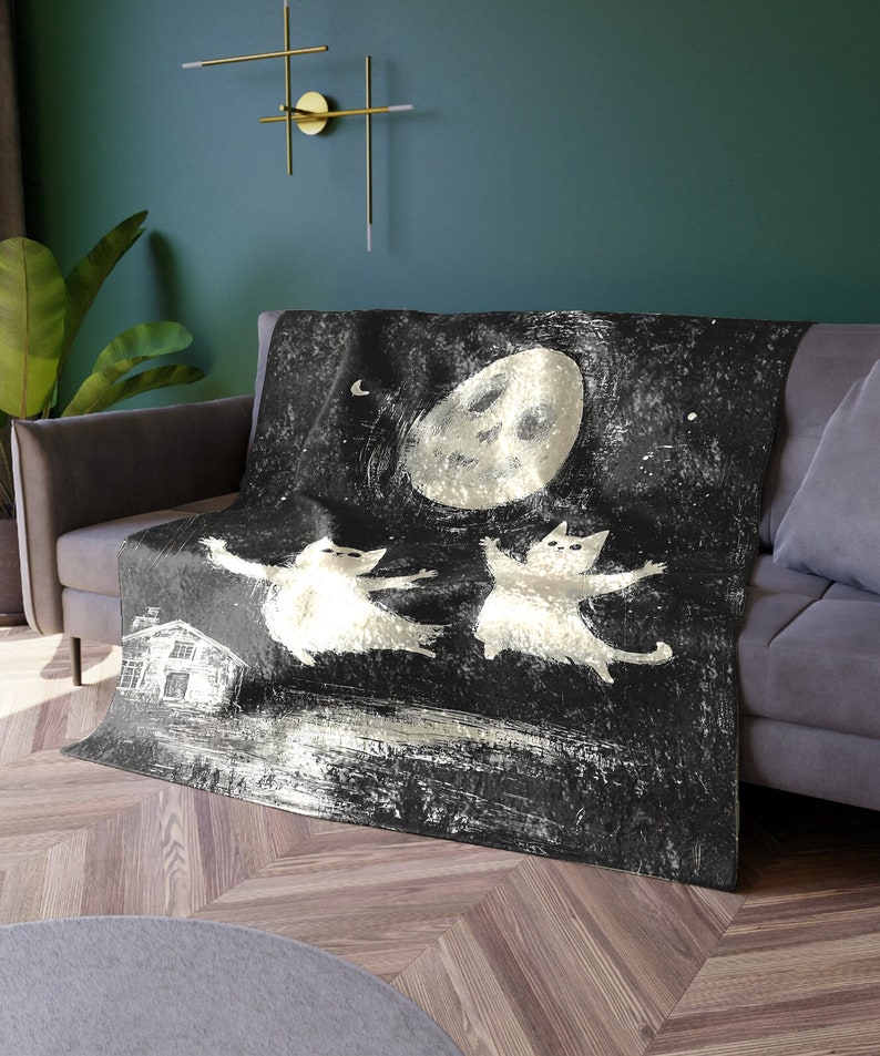 May include: A black and white throw blanket with a whimsical design of two cats dancing in front of a large moon. The background is a dark starry night.