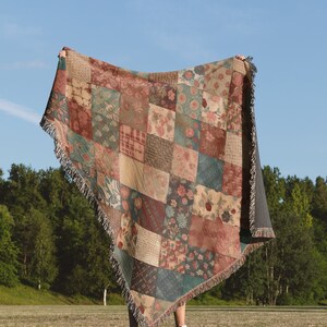 May include: A person holding a large, colourful patchwork throw blanket with a fringe border. The blanket is made of various fabrics with floral and geometric patterns in shades of red, brown, green, and beige.