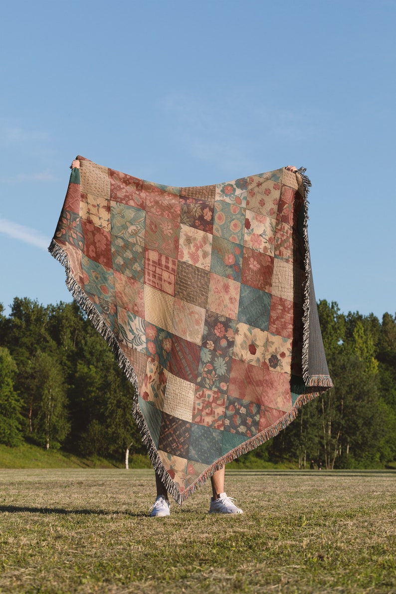 May include: A person holding a large, colourful patchwork throw blanket with a fringe border. The blanket is made of various fabrics with floral and geometric patterns in shades of red, brown, green, and beige.
