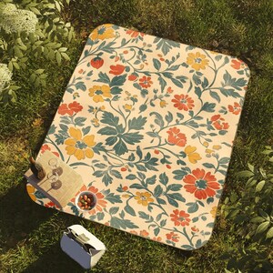 May include: A picnic blanket with a floral pattern in yellow, orange, and teal on a cream background. The blanket is on a grassy surface, with a small wooden serving board, wine glasses, and a cooler nearby. A perfect accessory for outdoor dining.