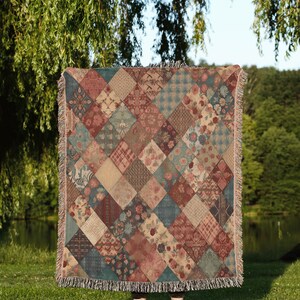 May include: A woven throw blanket with a patchwork design featuring various floral patterns in shades of red, blue, and beige. The blanket has a fringed edge.