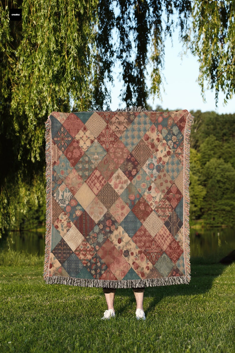 May include: A woven throw blanket with a patchwork design featuring various floral patterns in shades of red, blue, and beige. The blanket has a fringed edge.