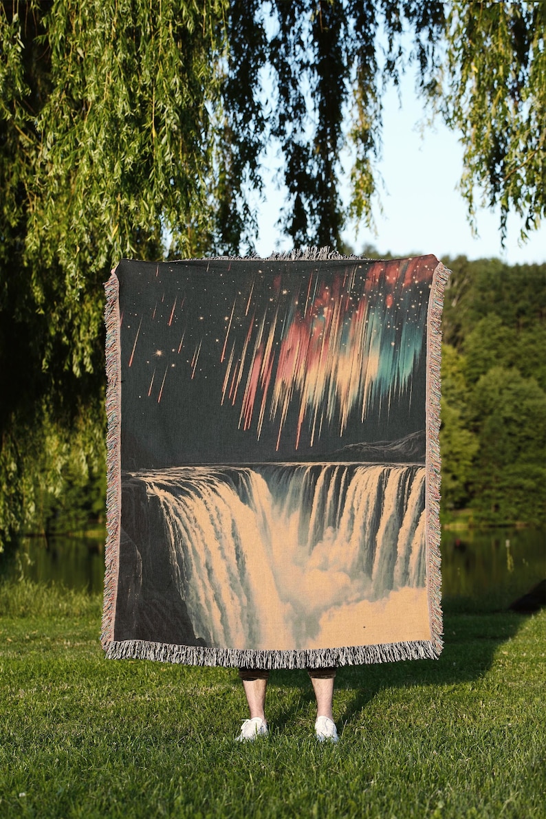 May include: A woven tapestry featuring a colorful aurora borealis and a waterfall. The tapestry is dark blue with streaks of pink, orange, green, and blue. The waterfall is white and cascading down a dark cliff.
