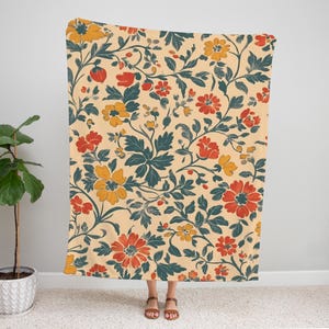May include: A floral patterned blanket featuring a cream background with red, yellow, and teal flowers and leaves. The blanket is held up by a person. The blanket is approximately 60 inches wide and 80 inches long.