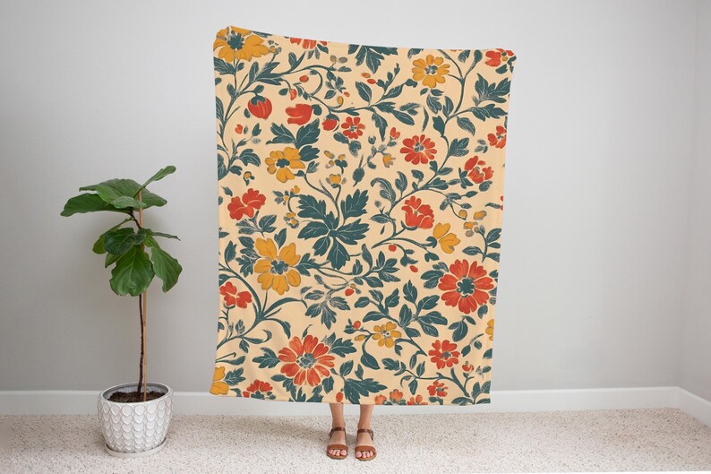 May include: A floral patterned blanket featuring a cream background with red, yellow, and teal flowers and leaves. The blanket is held up by a person. The blanket is approximately 60 inches wide and 80 inches long.