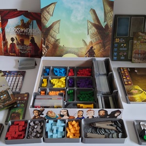 May include: A board game organiser with multiple compartments for storing game pieces, cards, and other components. The organiser is made of grey plastic and has a white background. The game is called "Works of Wonder: Architects of the Modern World".