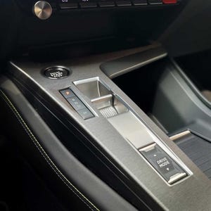 Può includere: Primo piano dell'interno di un'auto che mostra un cambio di marcia argentato con un pulsante di modalità di guida etichettato "Drive Mode". Il cambio di marcia ha pulsanti per "P", "R", "N", "D" e "M".