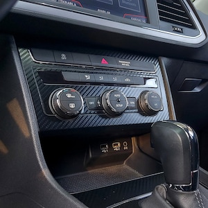 Puede incluir: Un salpicadero de coche negro con un patr&oacute;n de fibra de carbono. El salpicadero tiene varios botones, incluyendo "OFF", "AUTO", "SYNC" y "AC". Tambi&eacute;n hay dos puertos USB y una toma de auriculares.