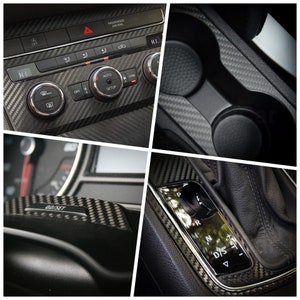 Puede incluir: Primer plano del interior de un coche con detalles de fibra de carbono. La imagen muestra el salpicadero, la palanca de cambios y los portavasos. El salpicadero tiene botones etiquetados como "HI", "OFF", "AUTO", "SETUP" y "SYNC". La palanca de cambios tiene las letras "P", "R", "N", "D/S" y un signo m&aacute;s y menos. Los portavasos est&aacute;n vac&iacute;os.