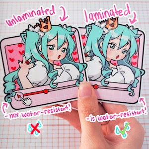 K&ouml;nnte beinhalten: Zwei Aufkleber mit einem Anime-Charakter mit t&uuml;rkisfarbenen Haaren und einer Krone. Der Charakter befindet sich vor einem rosa Hintergrund mit Herzen. Ein Aufkleber ist mit "unlaminiert" und der andere mit "laminiert" beschriftet. Der laminierte Aufkleber ist wasserfest.