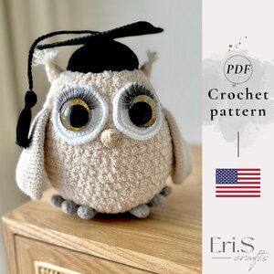 May include: A crocheted owl wearing a black graduation cap with a tassel. The owl has large, expressive eyes with long eyelashes and a beige body. The image includes the text "Crochet pattern" and the American flag.