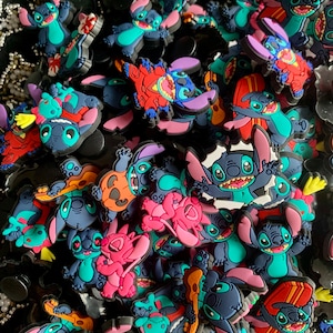 May include: A collection of colourful Stitch character charms, featuring various poses and designs, including Stitch playing guitar, surfing, and wearing a Hawaiian shirt. The charms are made of a soft, flexible material and are perfect for adding a touch of Disney magic to your belongings.