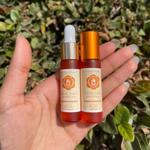 May include: Two small orange glass bottles with gold caps and droppers. The bottles are labeled with the text "Sacral Chakra swadisthana experience joy" and the logo "BLISS skincare".
