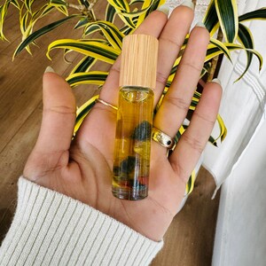 Pu&ograve; includere: Un flacone di vetro trasparente con tappo in legno, riempito di un liquido giallo e piccole pietre colorate. Il flacone &egrave; tenuto in una mano.