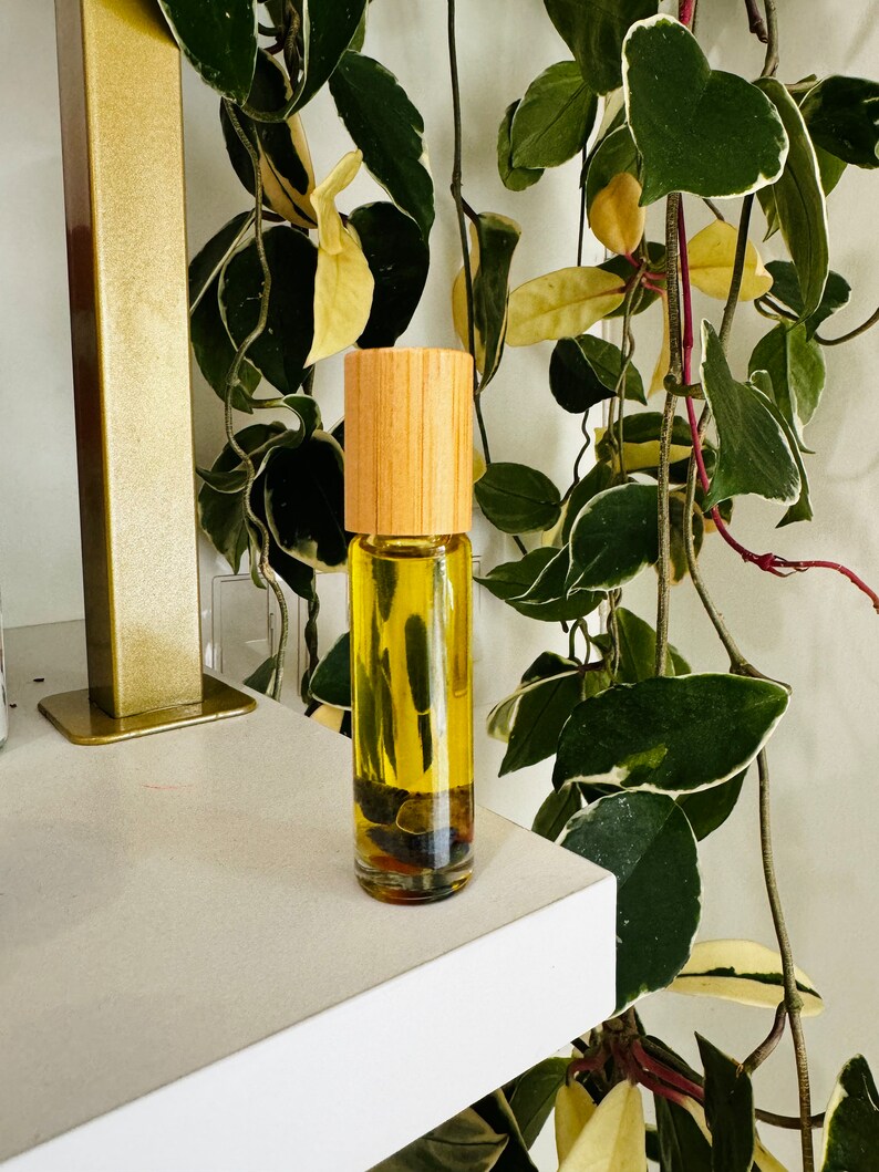 Pu&ograve; includere: Una bottiglia di vetro trasparente con un tappo di legno riempita di un liquido giallo. La bottiglia &egrave; appoggiata su uno scaffale bianco davanti a una pianta verde.