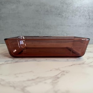 Puede incluir: Una fuente de horno rectangular de vidrio color ámbar. El plato tiene un diseño ligeramente acampanado y está hecho de vidrio transparente. El plato está vacío y listo para usar. Es un artículo de cocina.