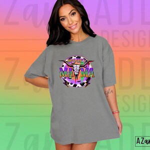 May include: A grey t-shirt with a colourful graphic that reads "Spooky Mama." The design includes a skull with horns, set against a purple, black, and white cow print. The shirt has a relaxed, oversized fit.