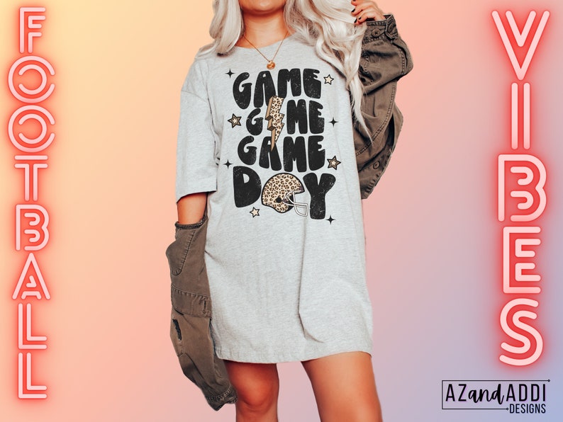 May include: A gray t-shirt with the text "Game Game Day" in black with a leopard print football helmet graphic. The text is in a retro font style with stars around it.