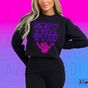 May include: A black cropped sweatshirt with the text "Stay Spooky" in a dripping neon purple and pink font. A skeleton hand with a pink outline is below the text.