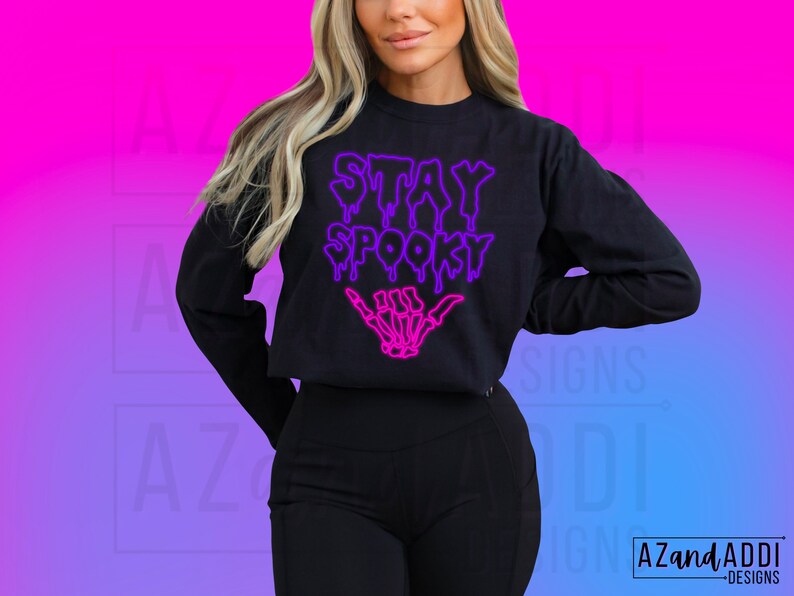 May include: A black cropped sweatshirt with the text "Stay Spooky" in a dripping neon purple and pink font. A skeleton hand with a pink outline is below the text.
