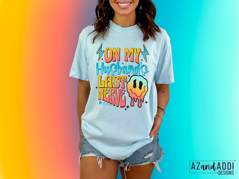 May include: A light blue t-shirt with the text "On My Husband's Last Nerve" in rainbow colors with a dripping smiley face graphic.