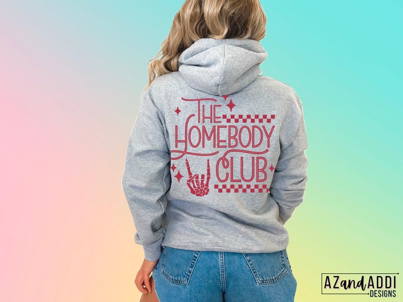 Puede incluir: Sudadera gris con capucha con el texto "The Homebody Club" en letras rojas con una mano de esqueleto haciendo un signo de rock and roll.