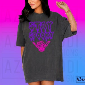 May include: A black t-shirt with a purple and pink graphic that says "Stay Spooky" with a skeleton hand giving a shaka sign.